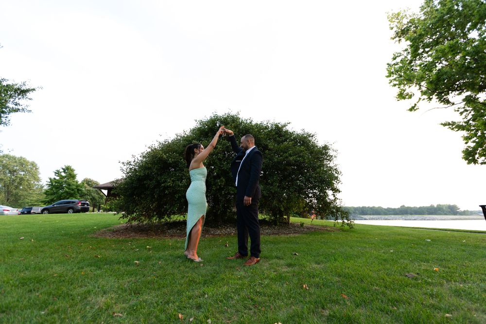 Couple shares a playful moment on grassy lawn near water.