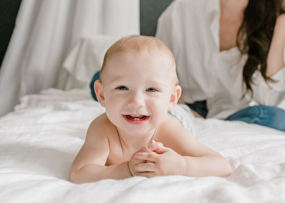 A joyful baby lying on white bedding with a bright happy smile.