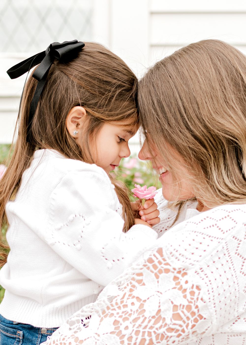 A tender moment shared between a little girl wearing a white sweater with a black bow and a woman in a lace top.