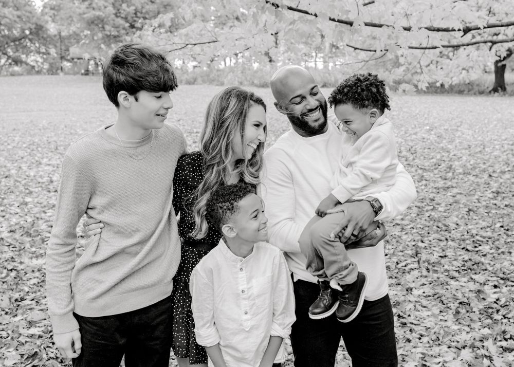 A joyful family of five shares a candid moment together outdoors in black and white.