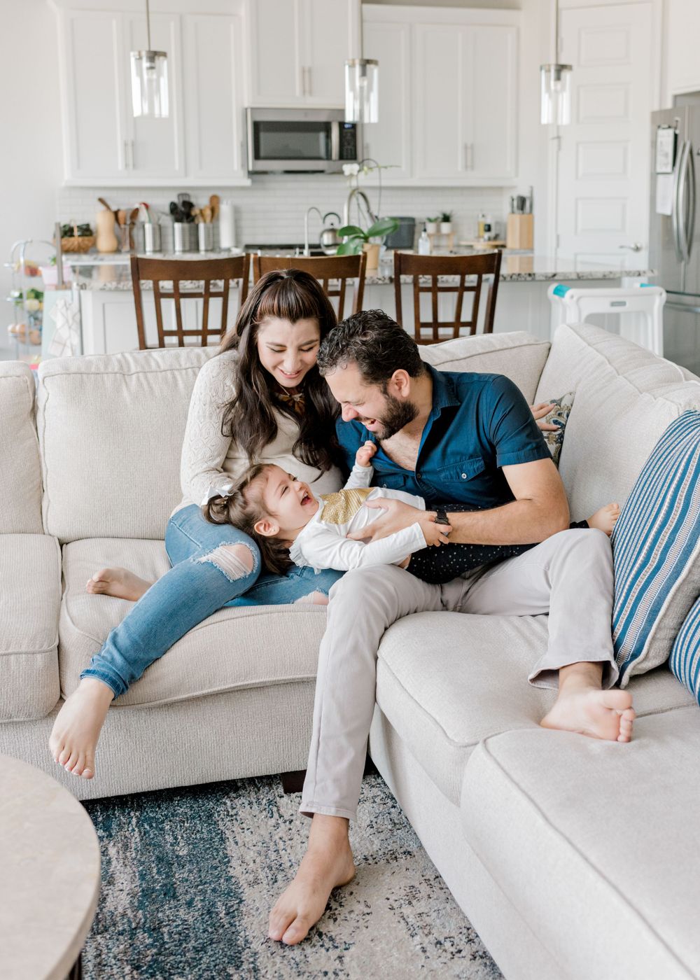 A relaxed family moment on a grey sectional sofa in a modern white kitchen.