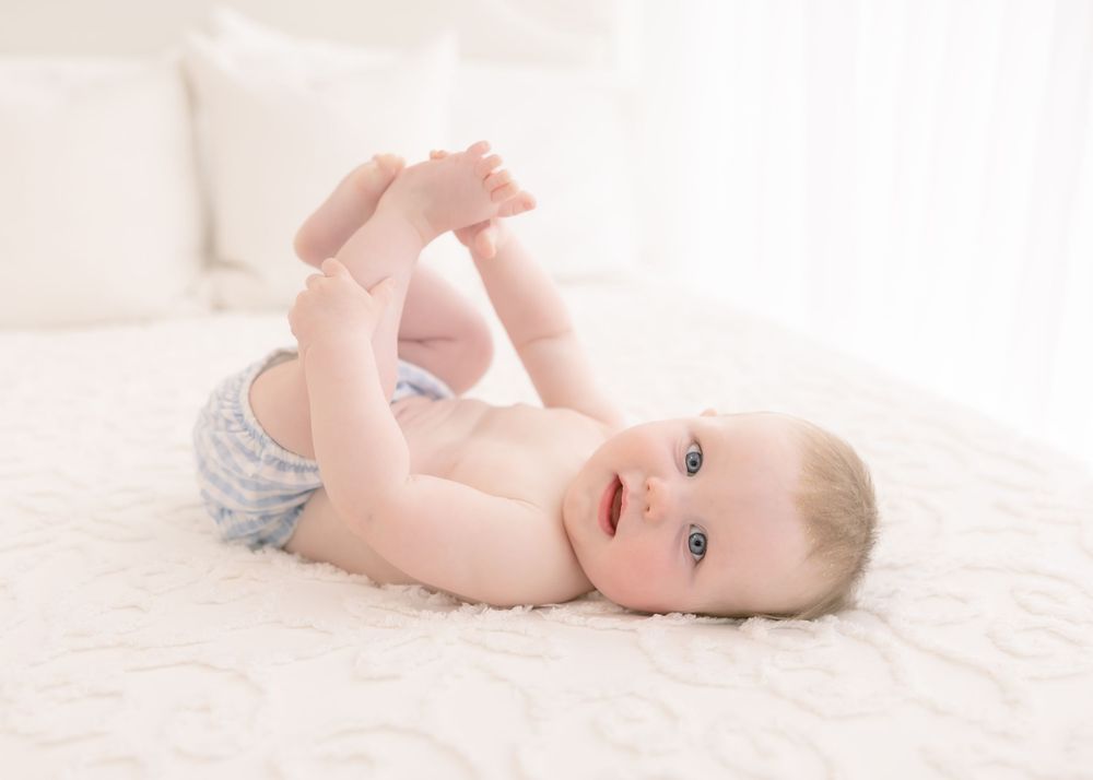 baby boy holding feet on white bed, sitter session, newborn photographer chattanooga, lookout mountain GA, red bank TN
