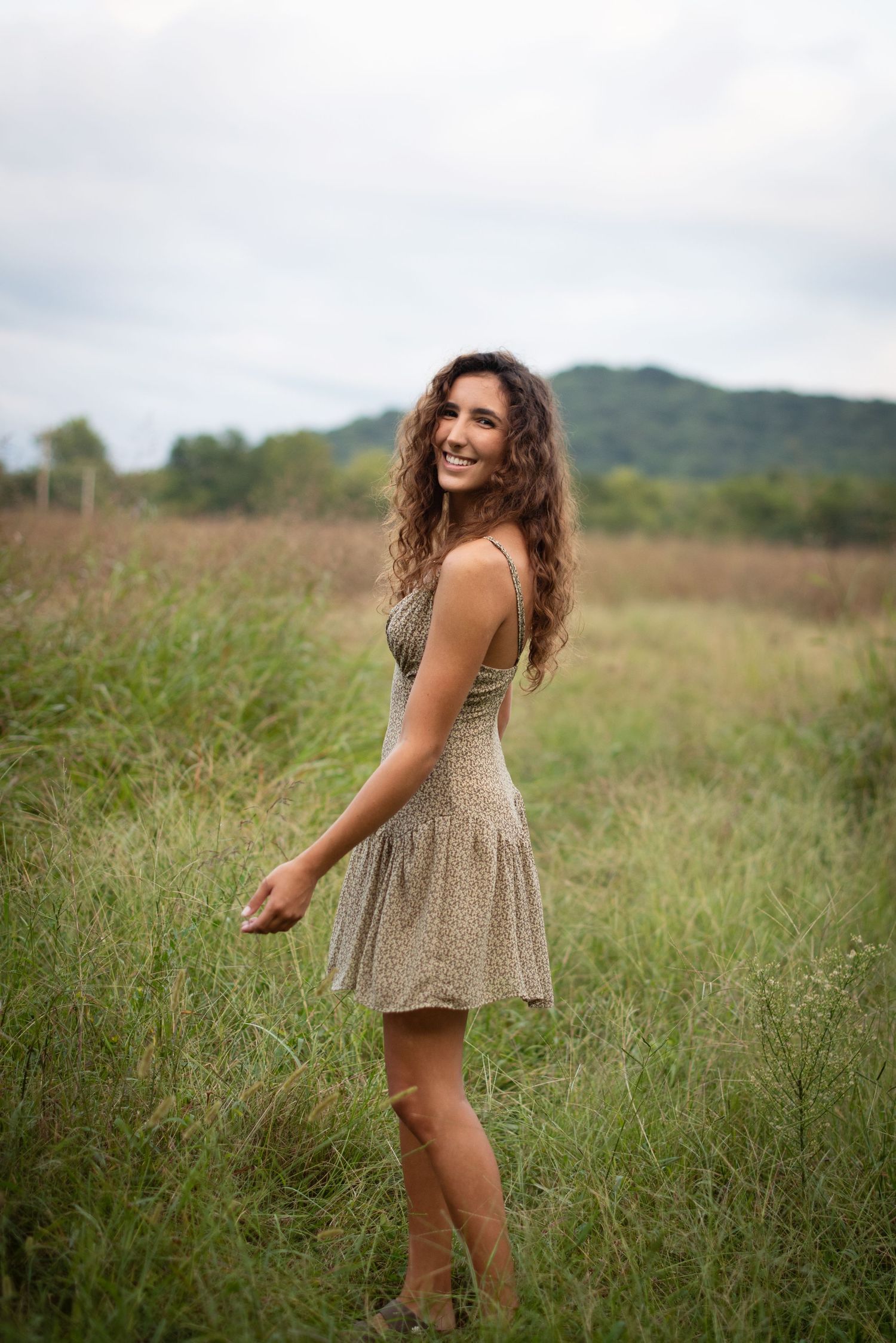 Floral dress captured in motion in a sunlit meadow with rolling hills in background.