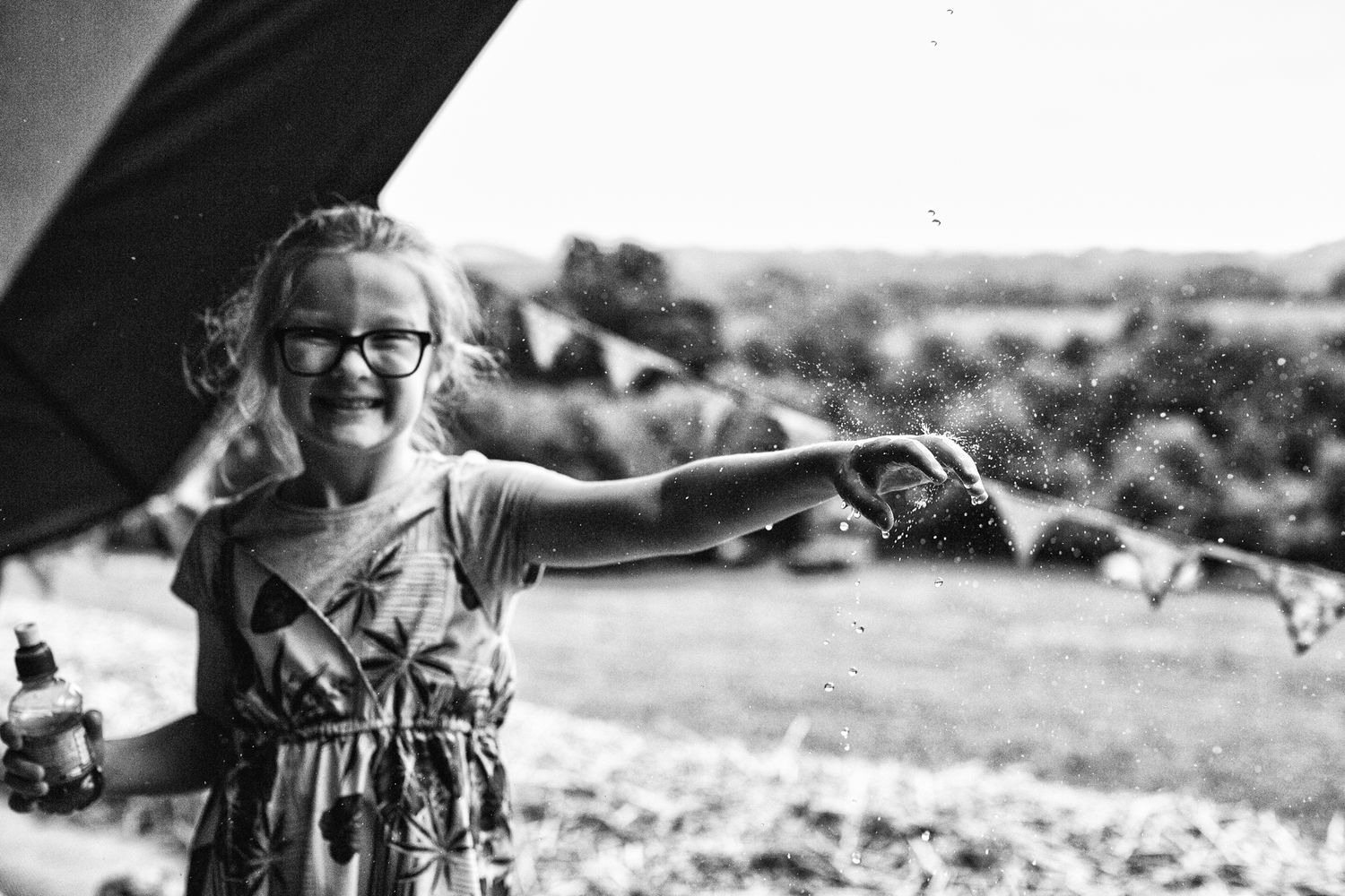 A young girl laughs as she hold her hand out from a canopy to collect falling rain drops