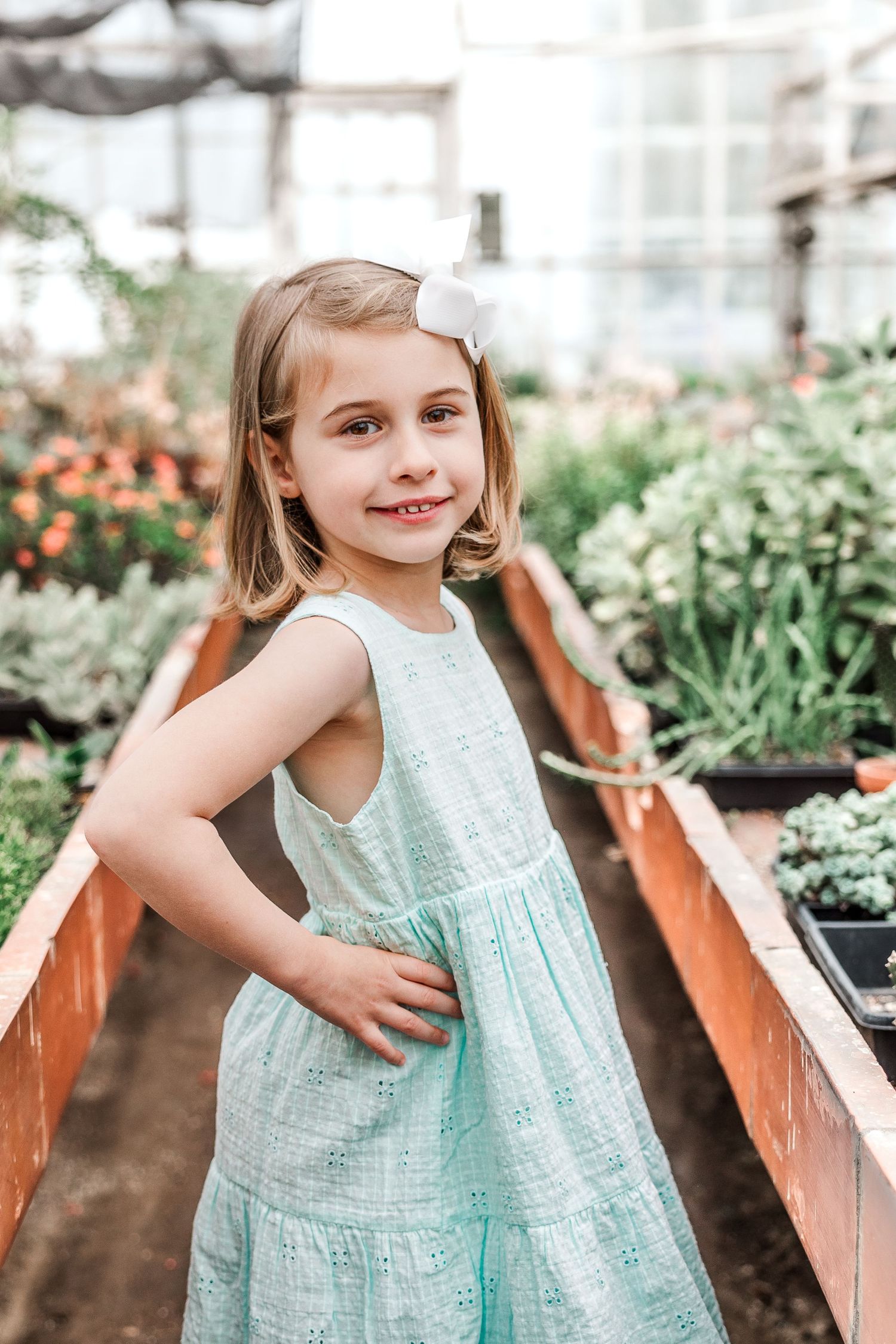 A figure in a mint eyelet dress poses between raised garden beds.