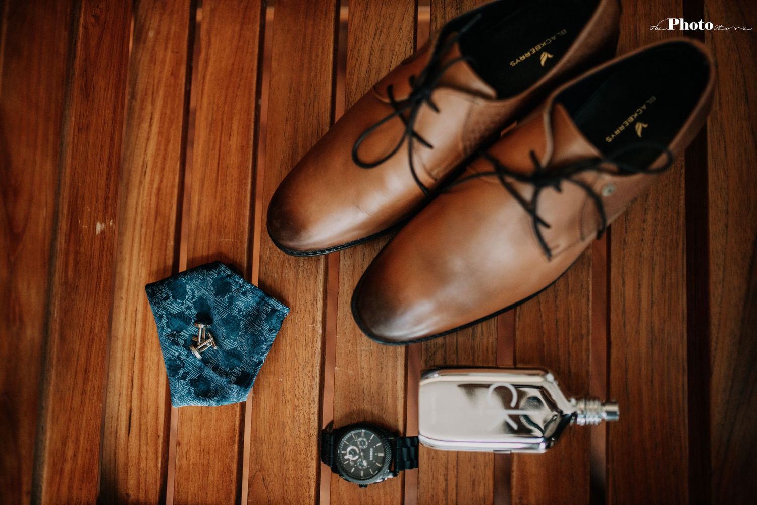 Brown leather dress shoes arranged on wooden floor with blue floral decor and accessories.