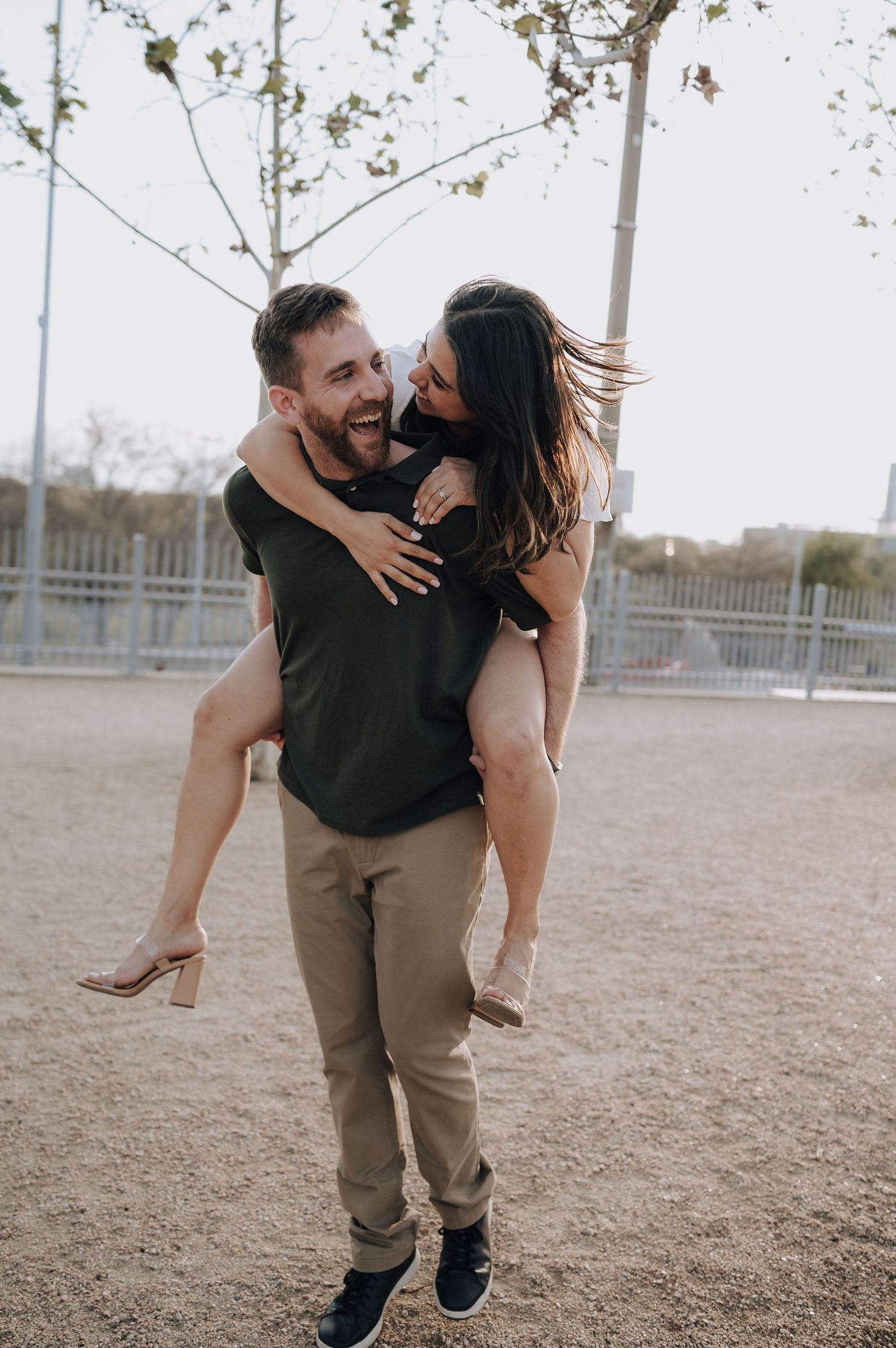 A playful piggyback ride between a couple in an outdoor setting with trees in the background.