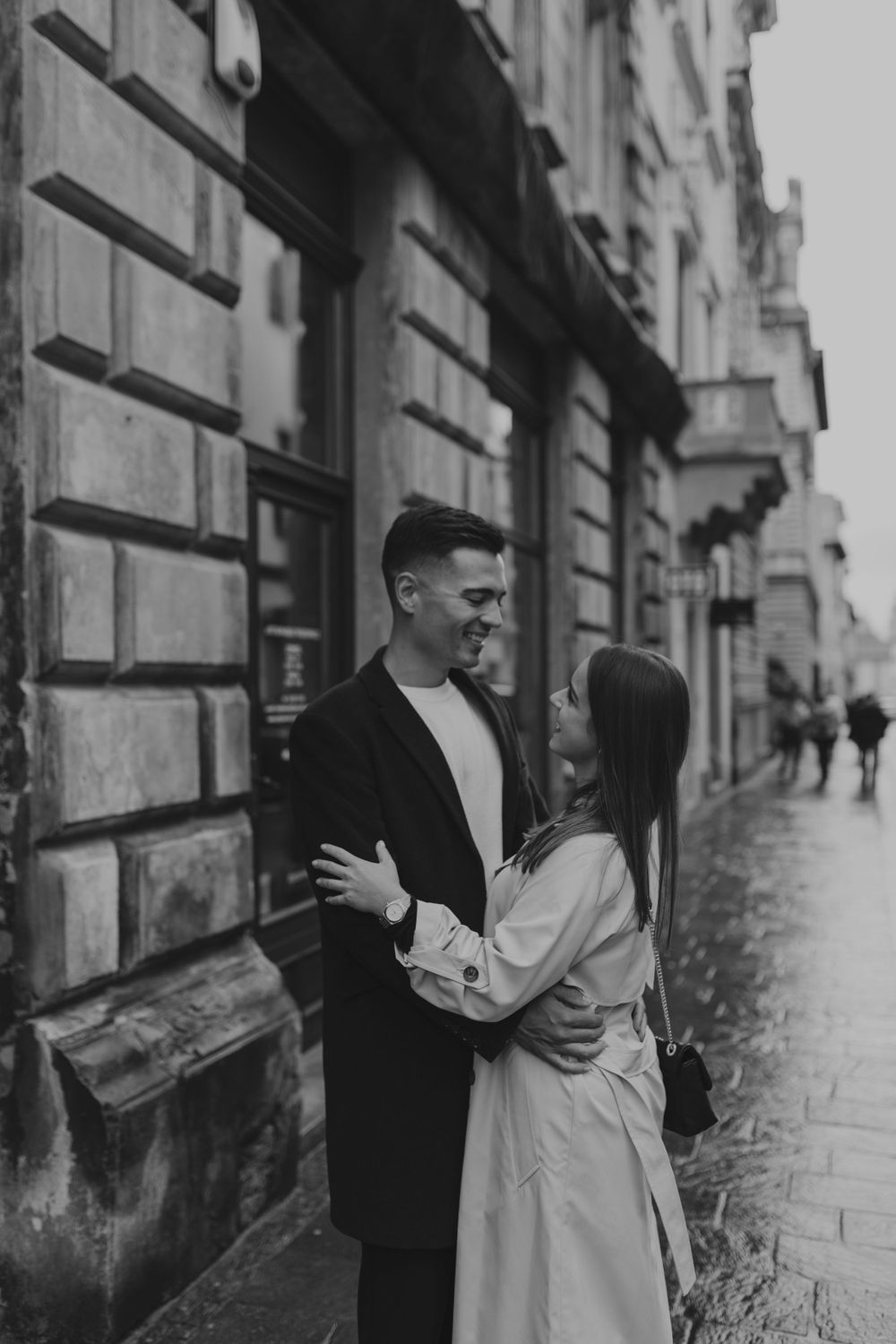 A romantic moment between two people on a rainy street beside historic stone buildings.