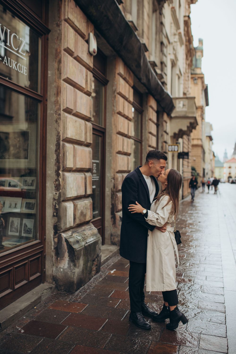 A tender moment between a couple outside a vintage storefront on a rainy day.
