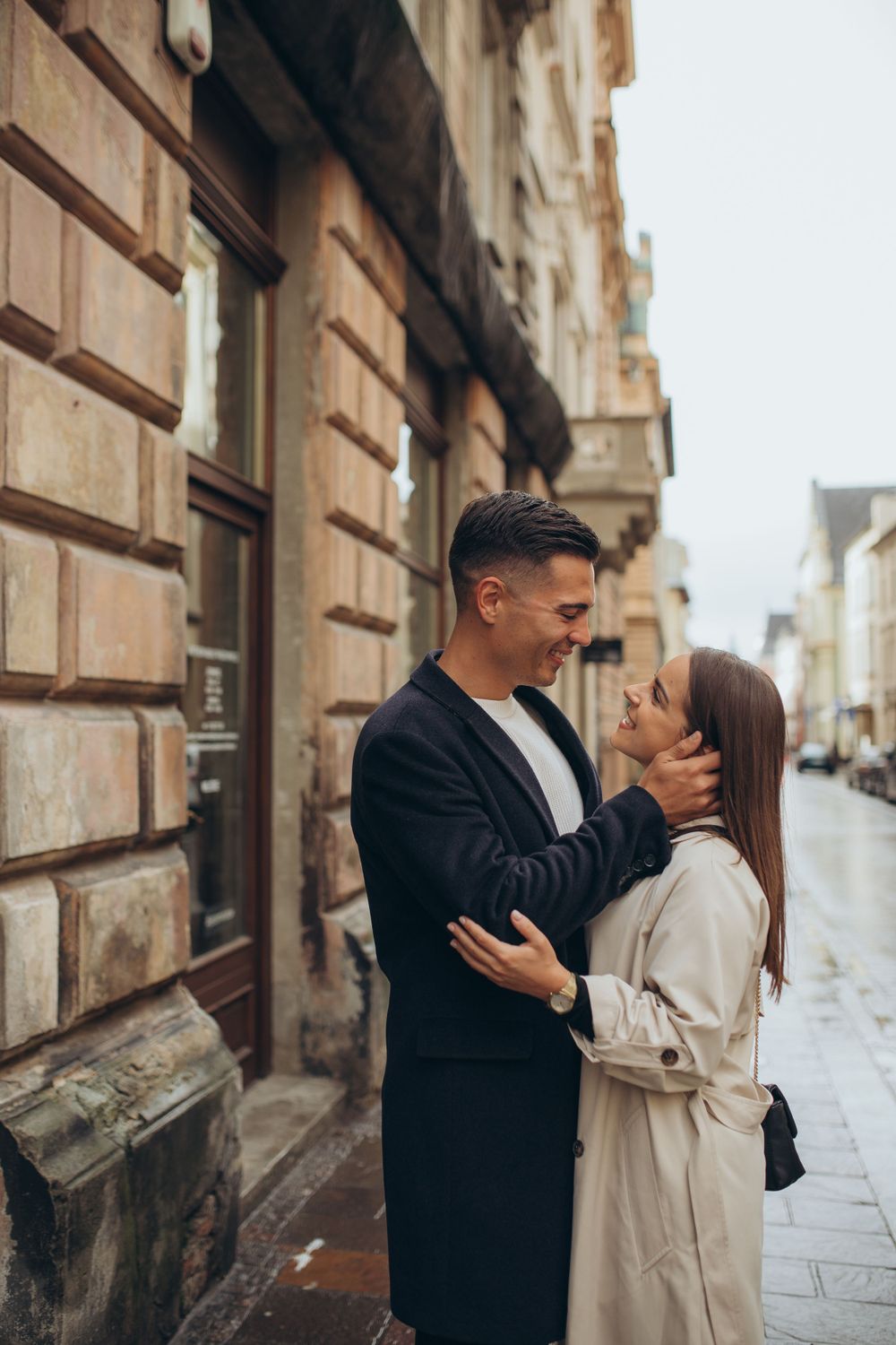 A romantic embrace captured on a historic European street with classical stone buildings.