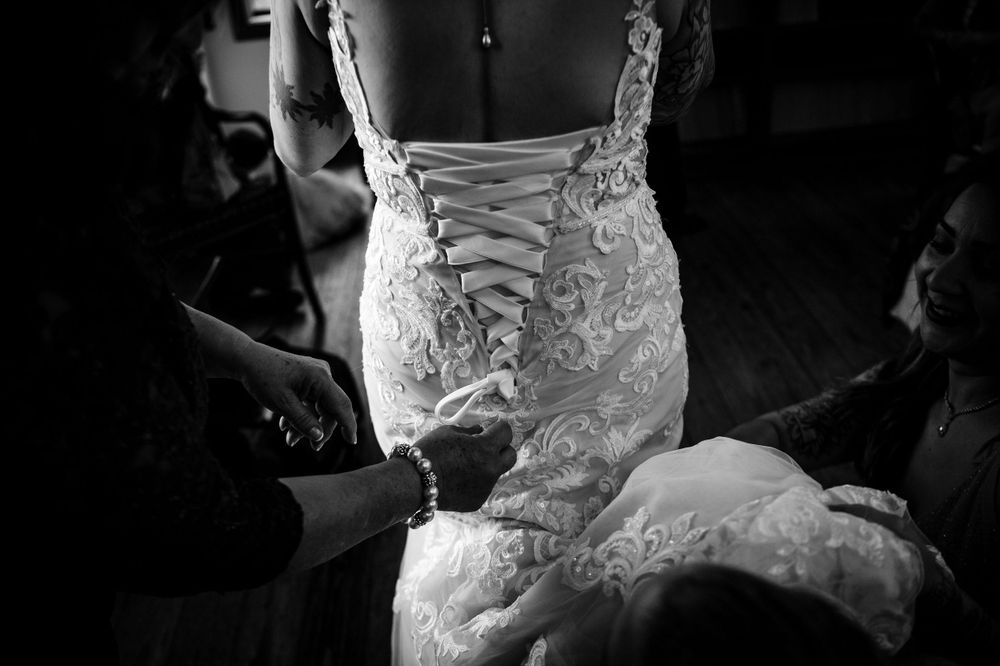 Black and white detail shot of intricate lace corset back being laced on wedding dress.