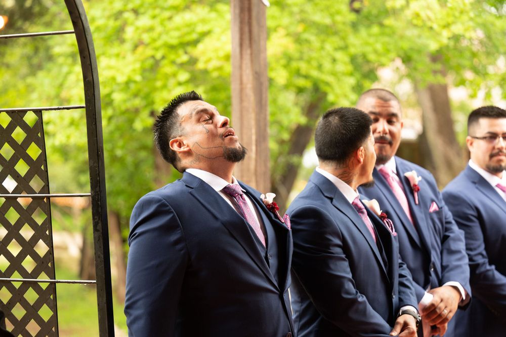 Wedding party members share joyful reactions under garden arbor during outdoor ceremony.