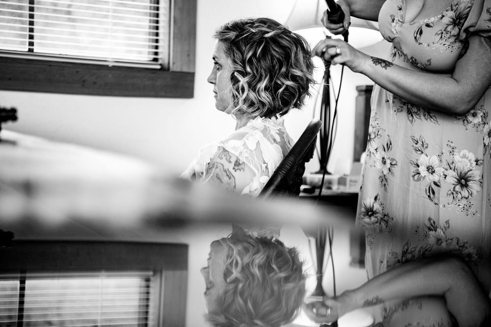 Black and white profile shot of wedding preparation with hairstyling in progress.