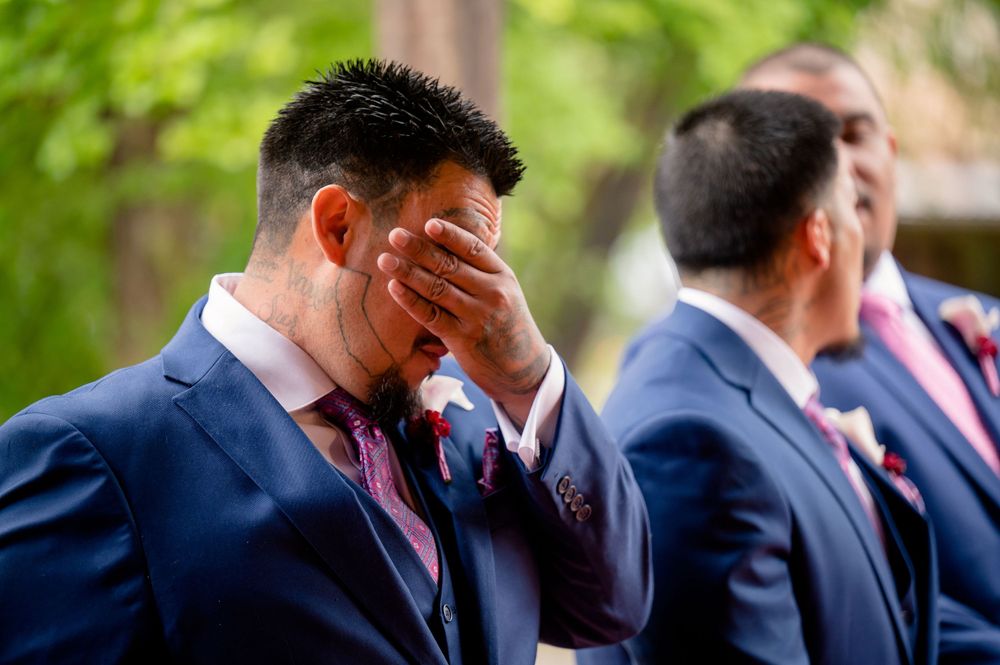 Emotional moment during outdoor wedding as groomsman wipes tears during ceremony.