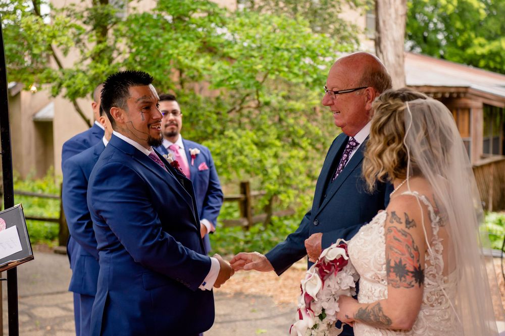 Wedding party exchanging handshakes during outdoor garden ceremony.
