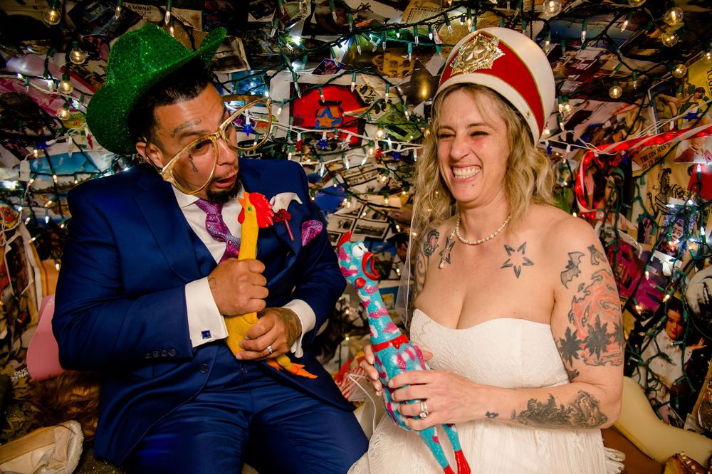 Wedding couple laughing while holding colorful retro toys under ceiling covered in decorations.