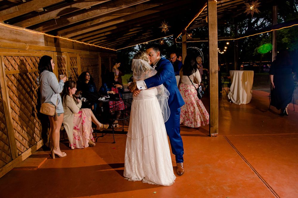 Wedding dance scene with bride in white gown on rustic wooden floor with guests watching.