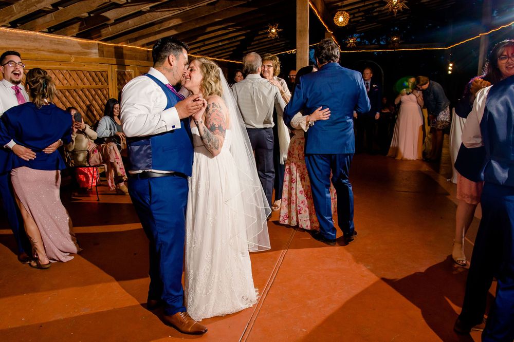 Couple shares intimate dance moment during wedding reception on rustic wooden dance floor.