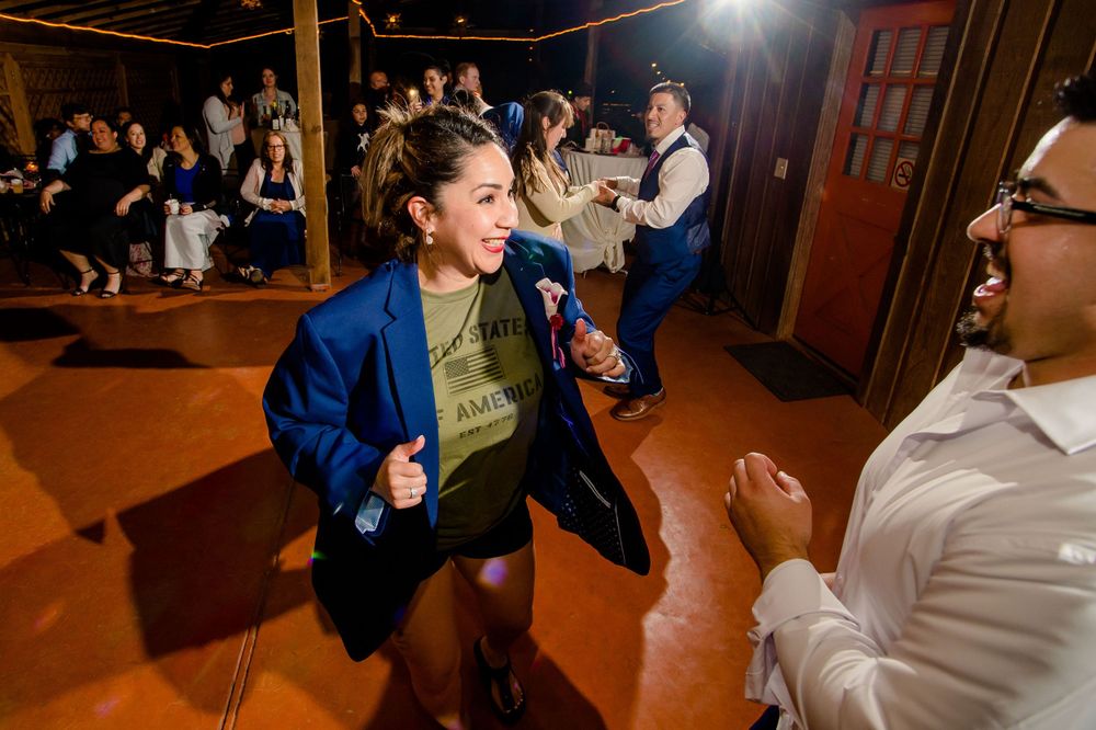 Wedding guests dancing enthusiastically at indoor reception with wooden ceiling.