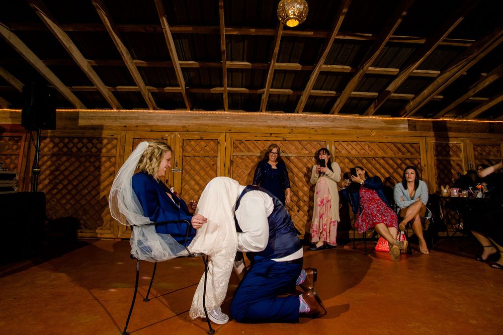Wedding party members perform traditional reception game with chairs on wooden dance floor.