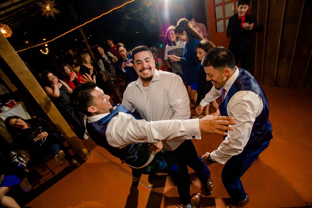 Groomsmen in blue vests lift and celebrate during lively wedding reception dance.