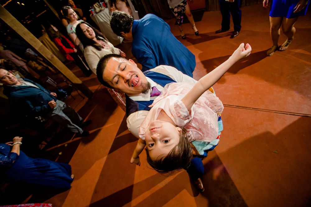 Couple performs dramatic dance dip during wedding reception on rustic dance floor.