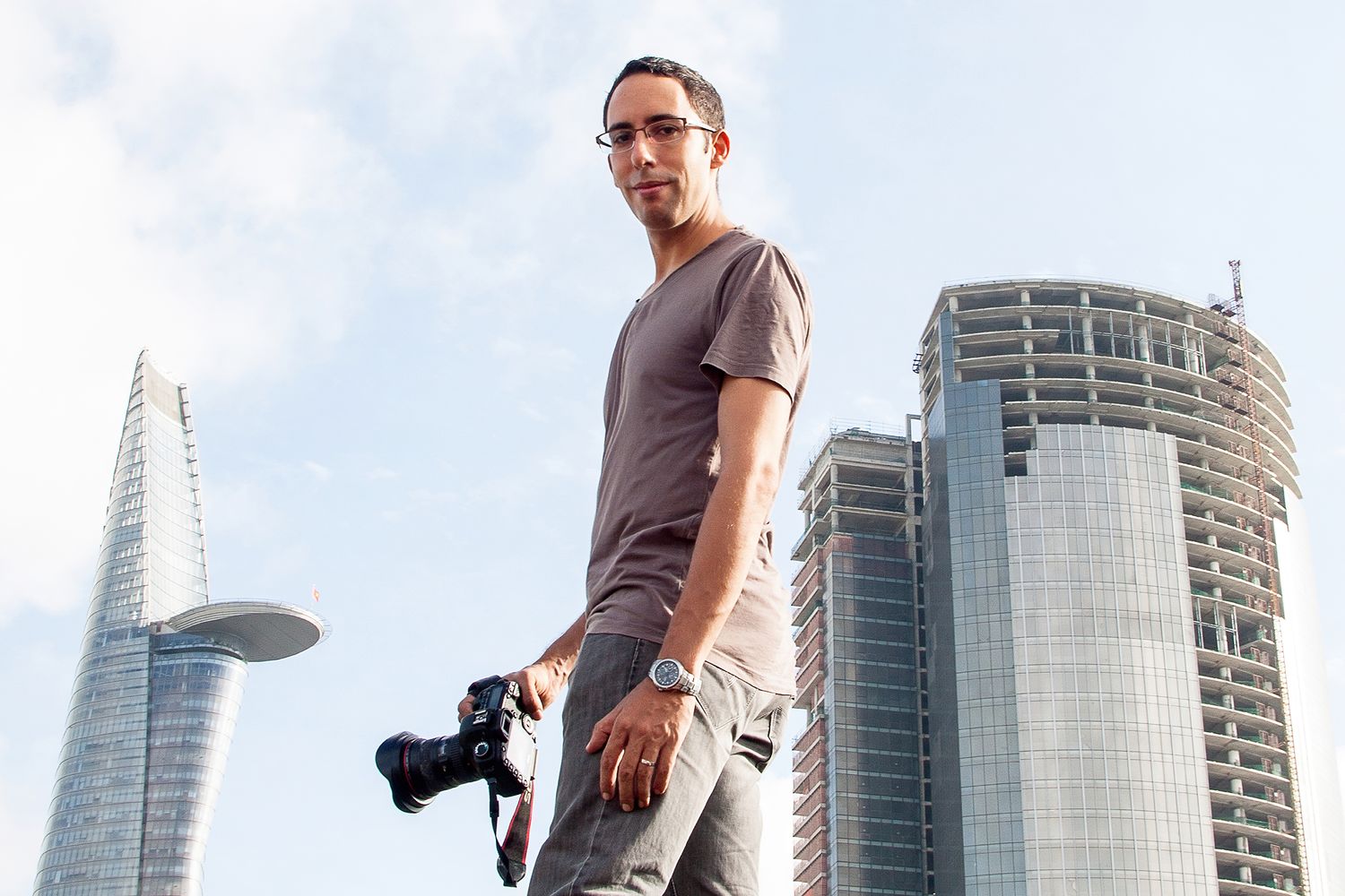 Photograph of photographer Adam Robert Young standing in front of Hochiminh City skyline holding a camera