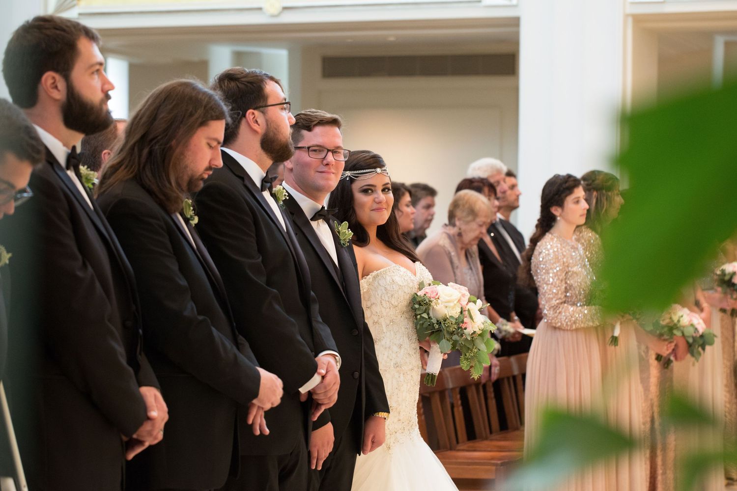 Wedding party lined up watching ceremony in formal black attire and blush gowns.