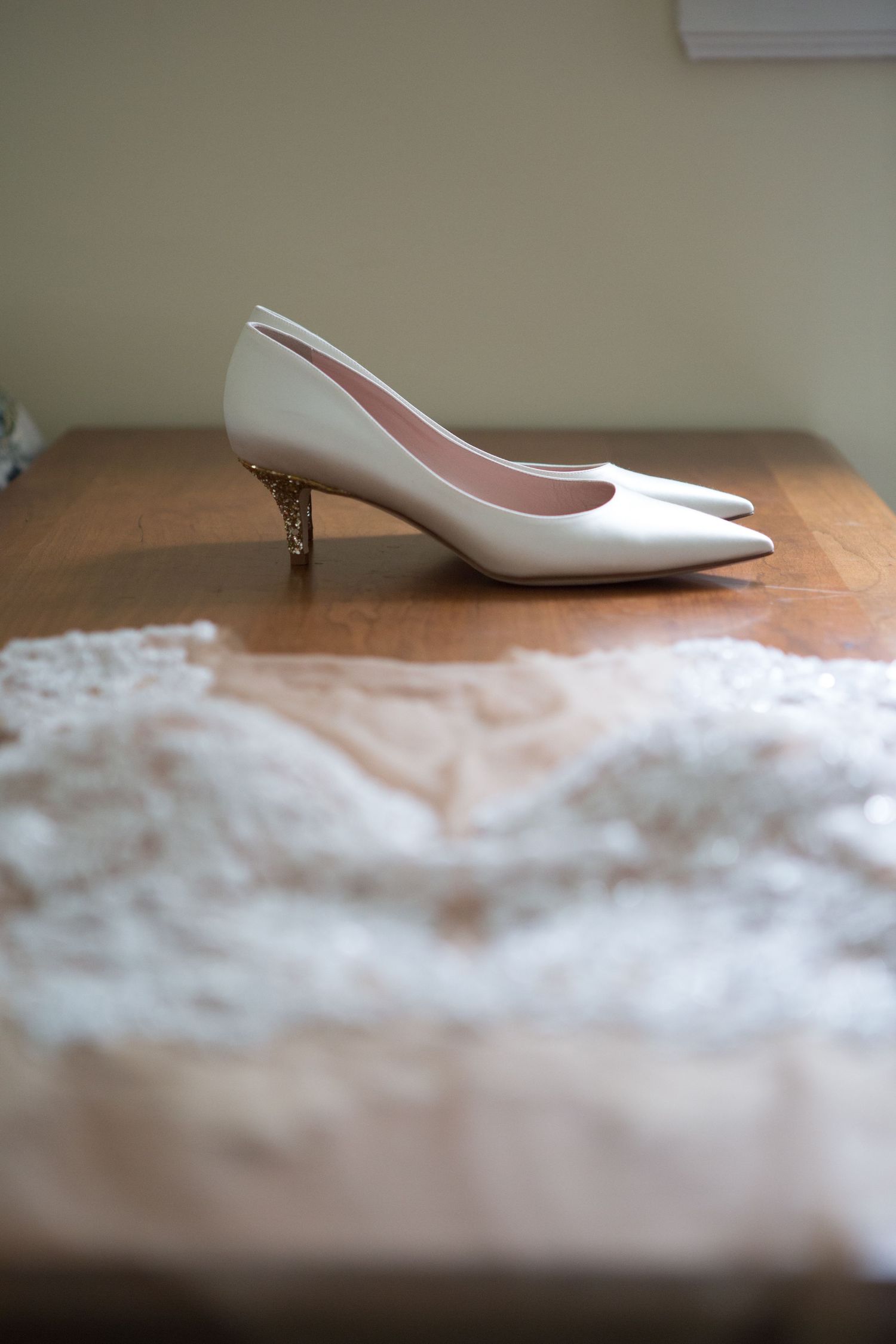 A white pointed-toe kitten heel pump displayed on a lace fabric surface.