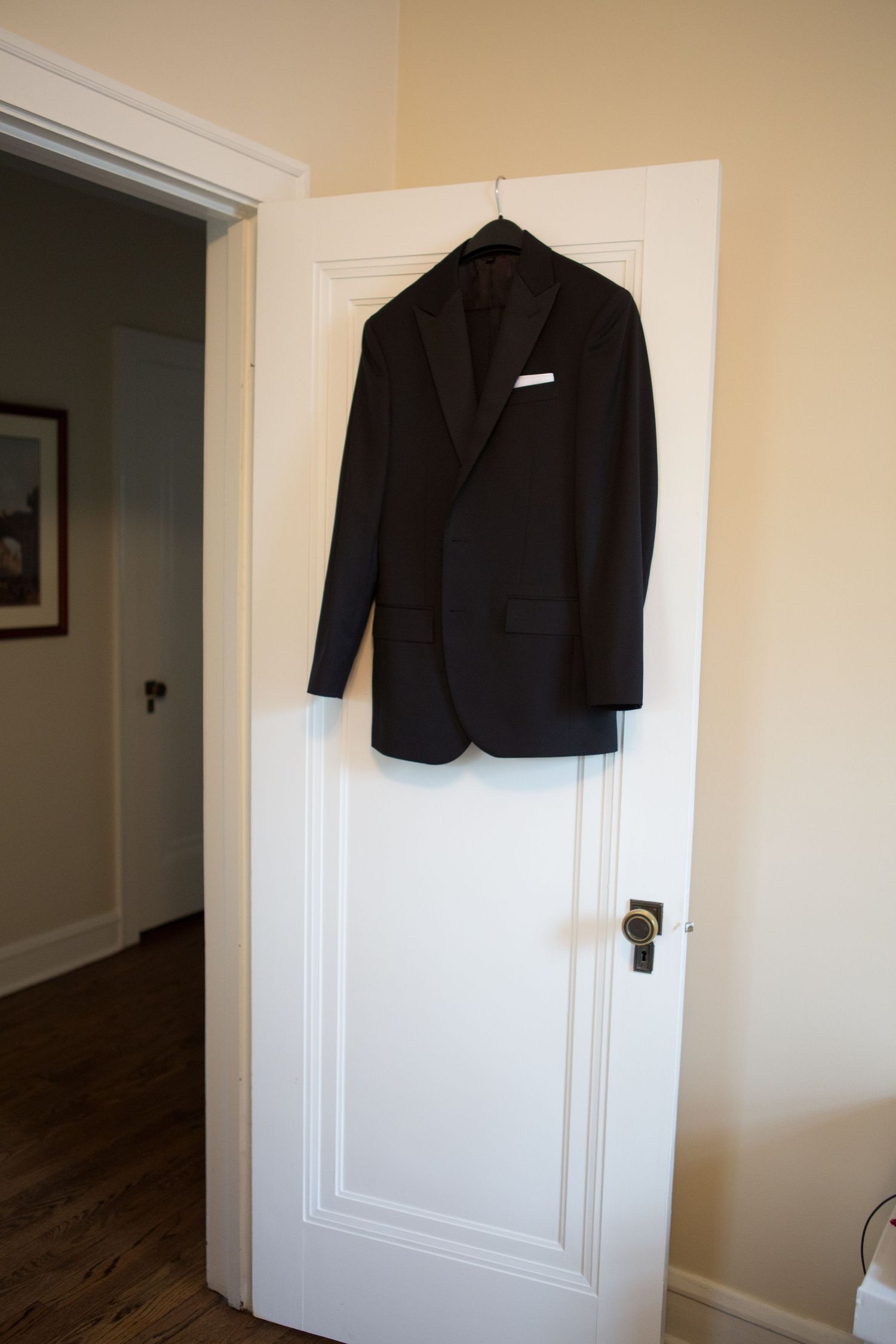 A classic black suit jacket hangs on a white wooden door in preparation for a formal event.