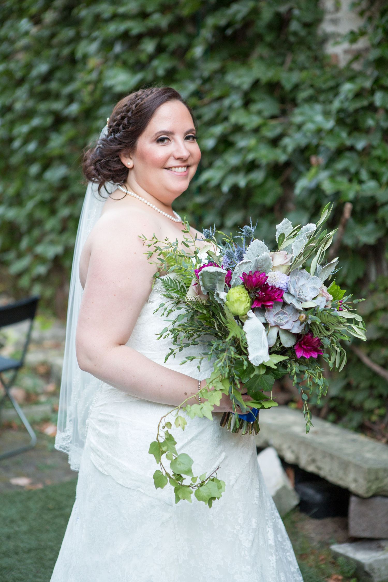 A person in a white wedding dress holds a vibrant bouquet featuring purple and white flowers with greenery.