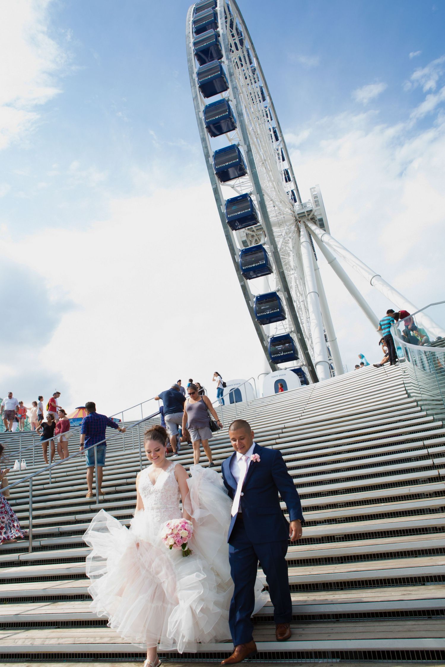 Newlyweds descend grand steps with a large Ferris wheel in the background.