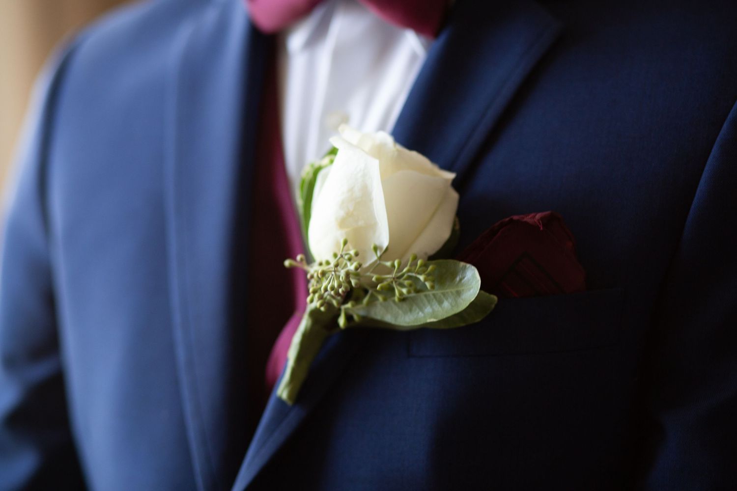 White rose and baby's breath boutonniere pinned to navy blue suit jacket.