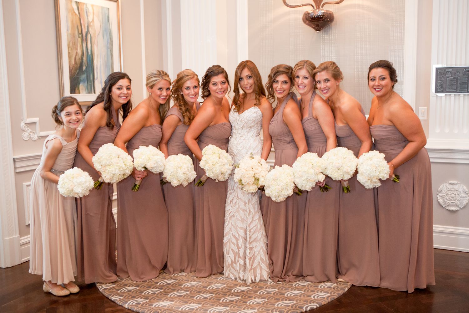 Wedding party poses with white bouquets wearing mauve bridesmaid dresses.