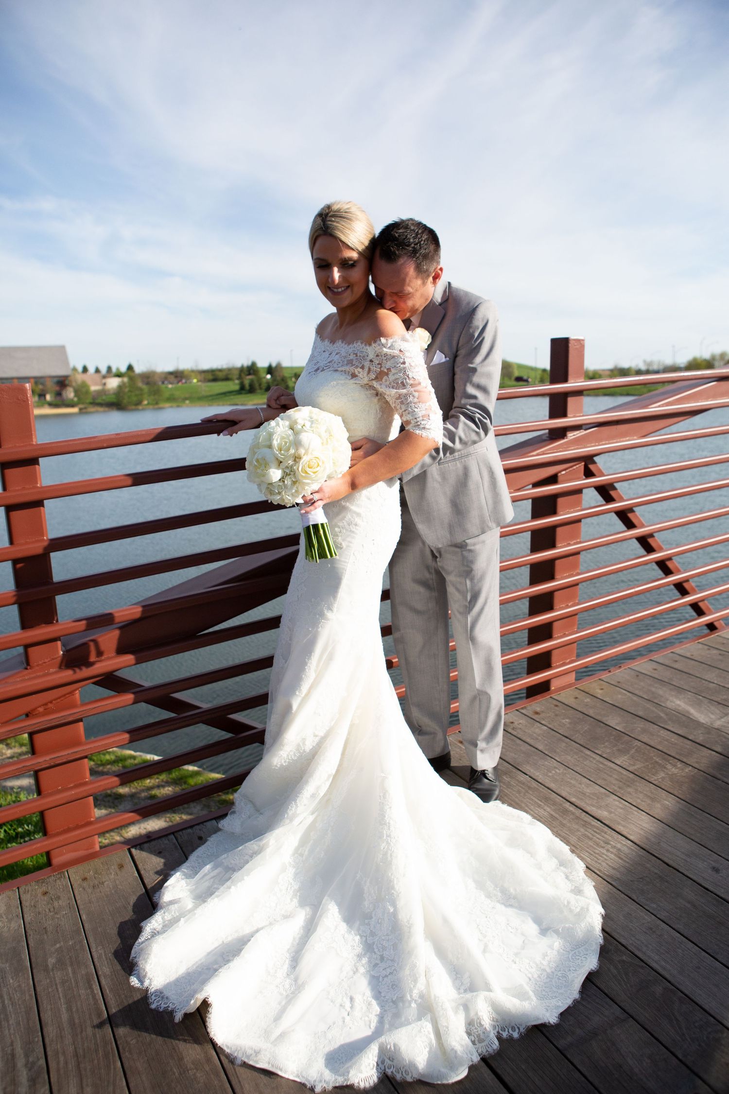 A romantic wedding moment on a wooden deck with a bride in a flowing white gown holding a bouquet.