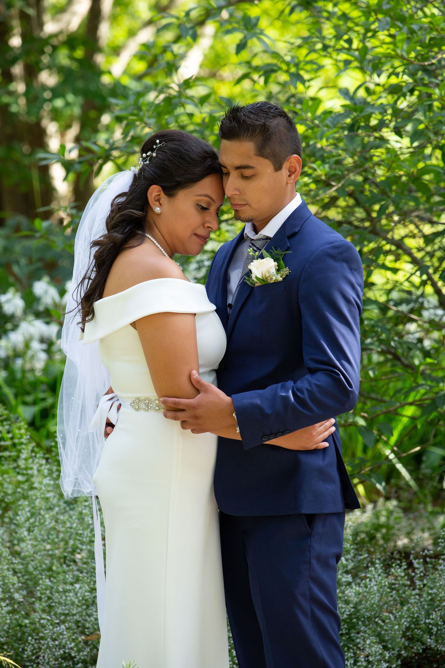 A tender wedding moment in a lush garden setting with greenery and white flowers.