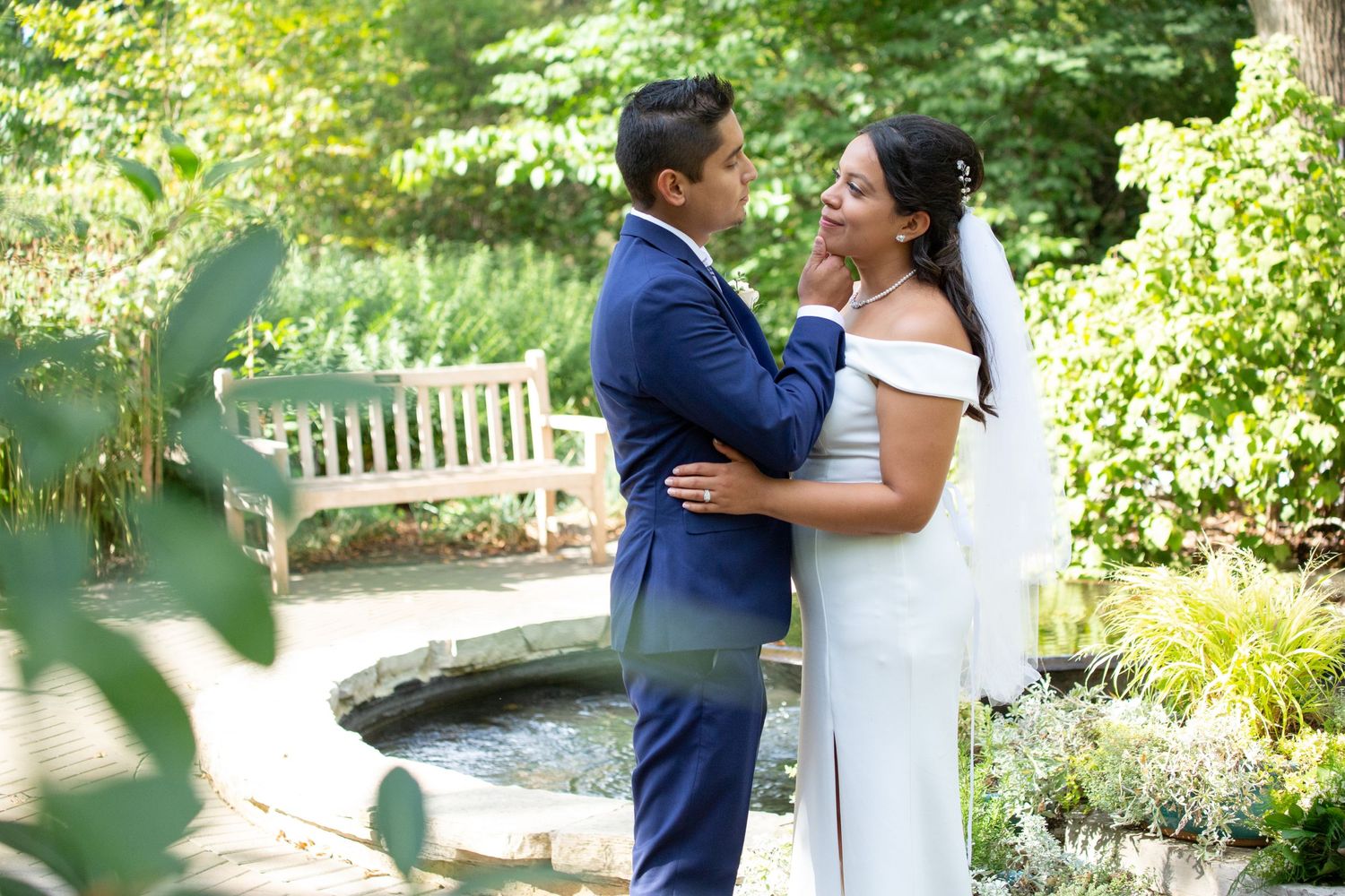 A romantic garden wedding portrait with beautiful natural greenery and a garden bench.