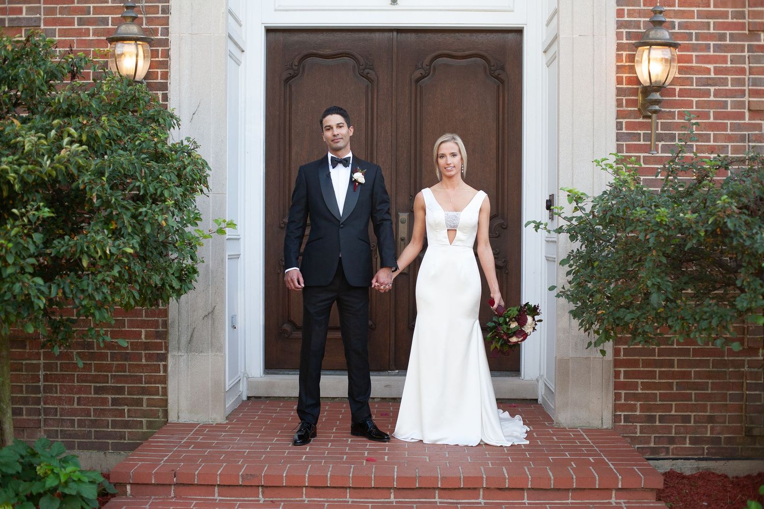 Wedding couple standing in front of classic brick church entrance with white columns.