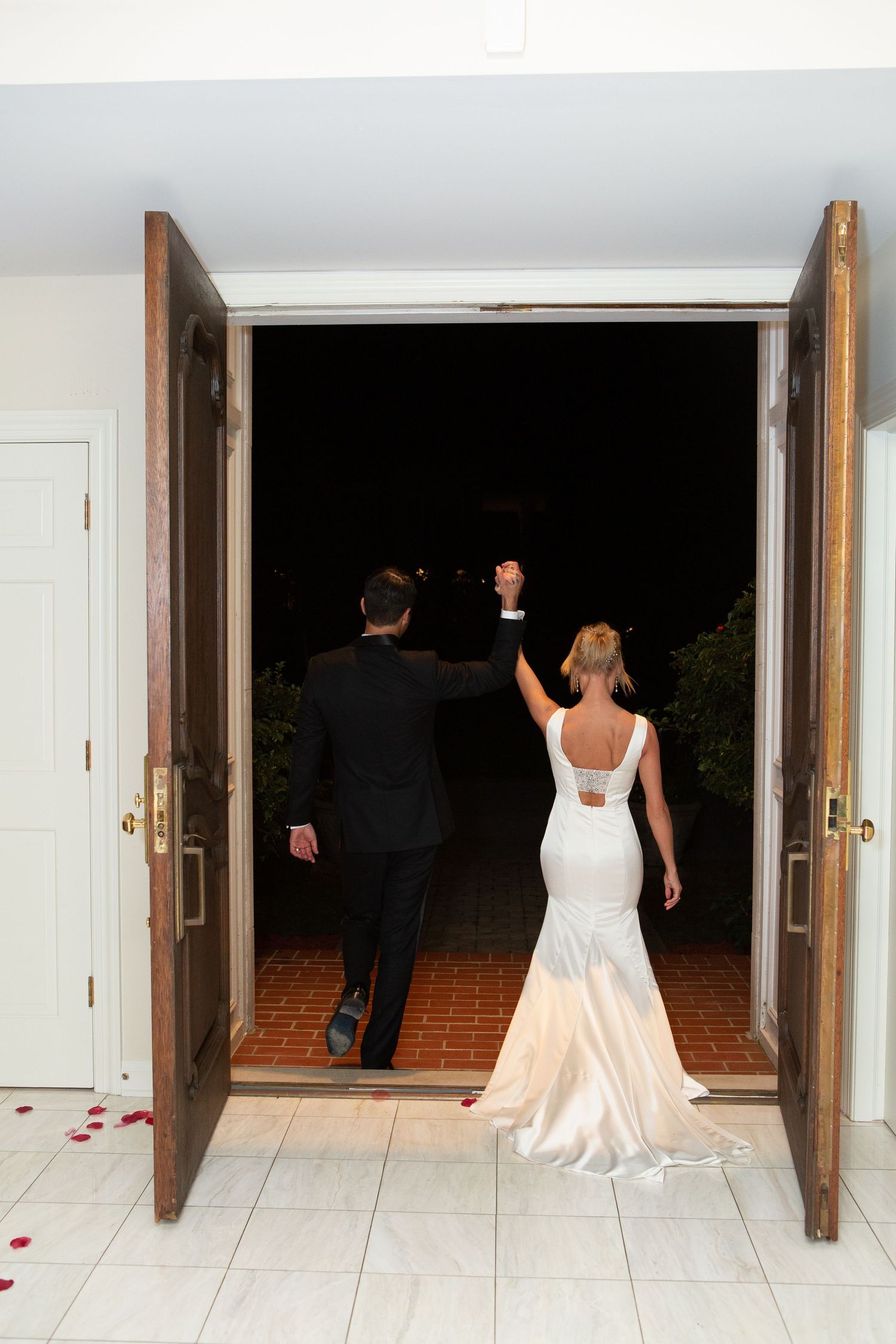 A couple exits through grand wooden doors, with the bride's dress trailing behind them.