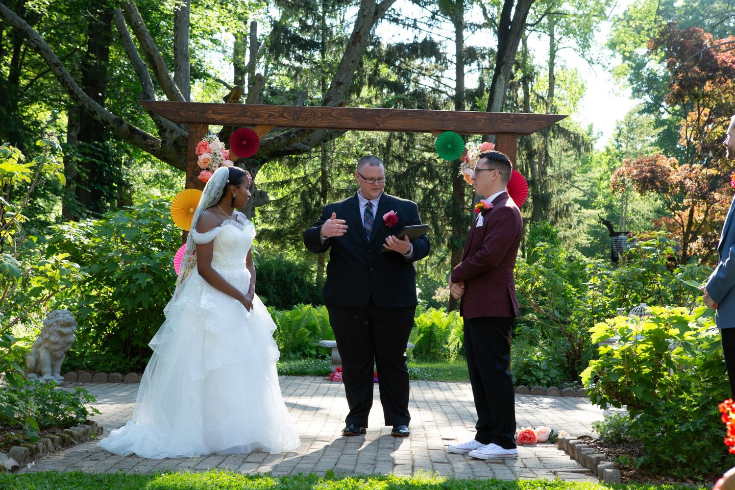 Outdoor wedding ceremony under wooden arbor surrounded by lush garden landscaping.