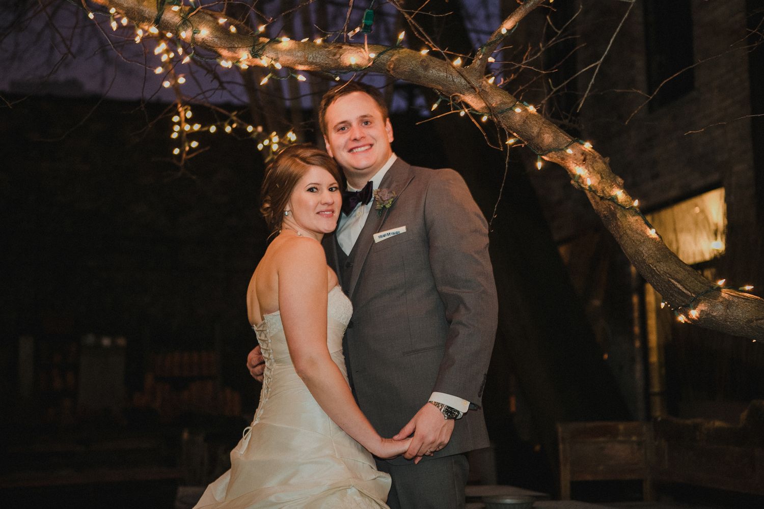 Romantic evening portrait under twinkling lights at wedding reception.