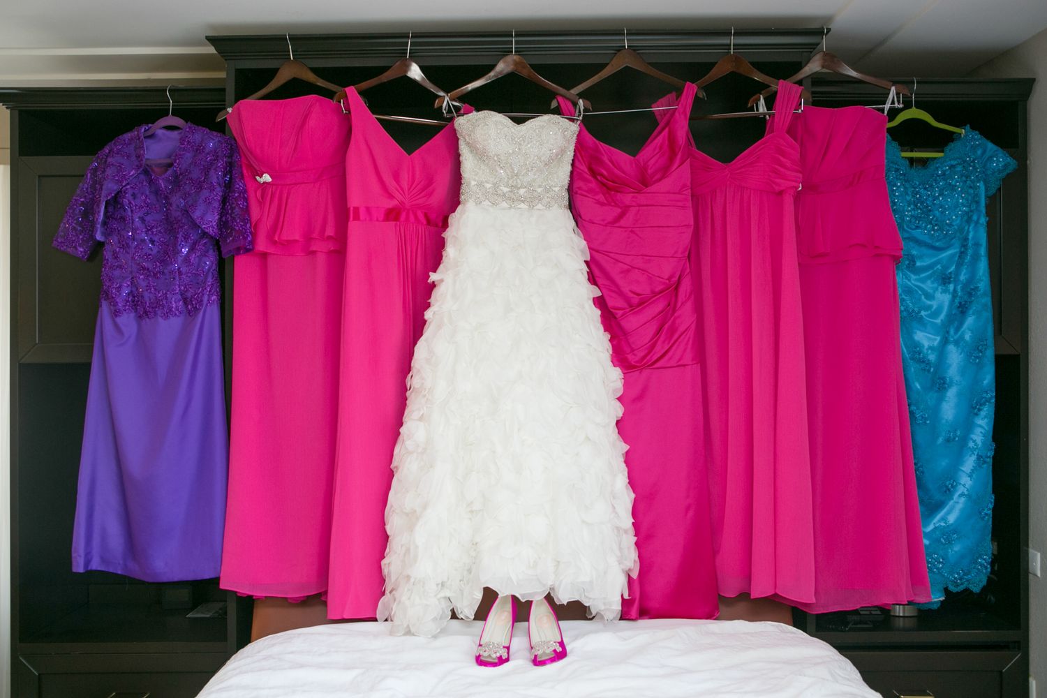 Colorful bridesmaid dresses and white wedding gown hanging in a row.