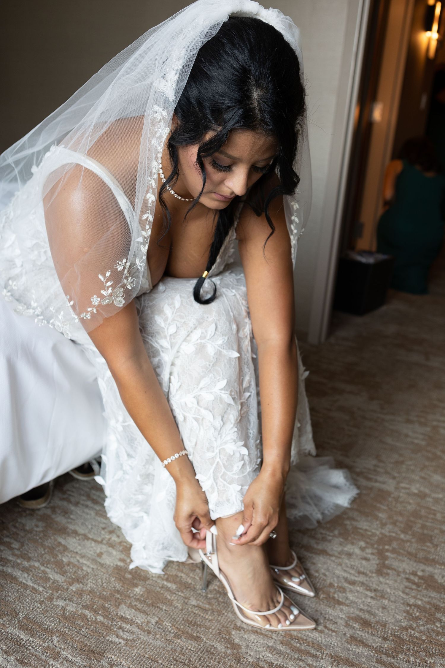 A bride in a lace veil adjusts her shoe strap while getting ready.