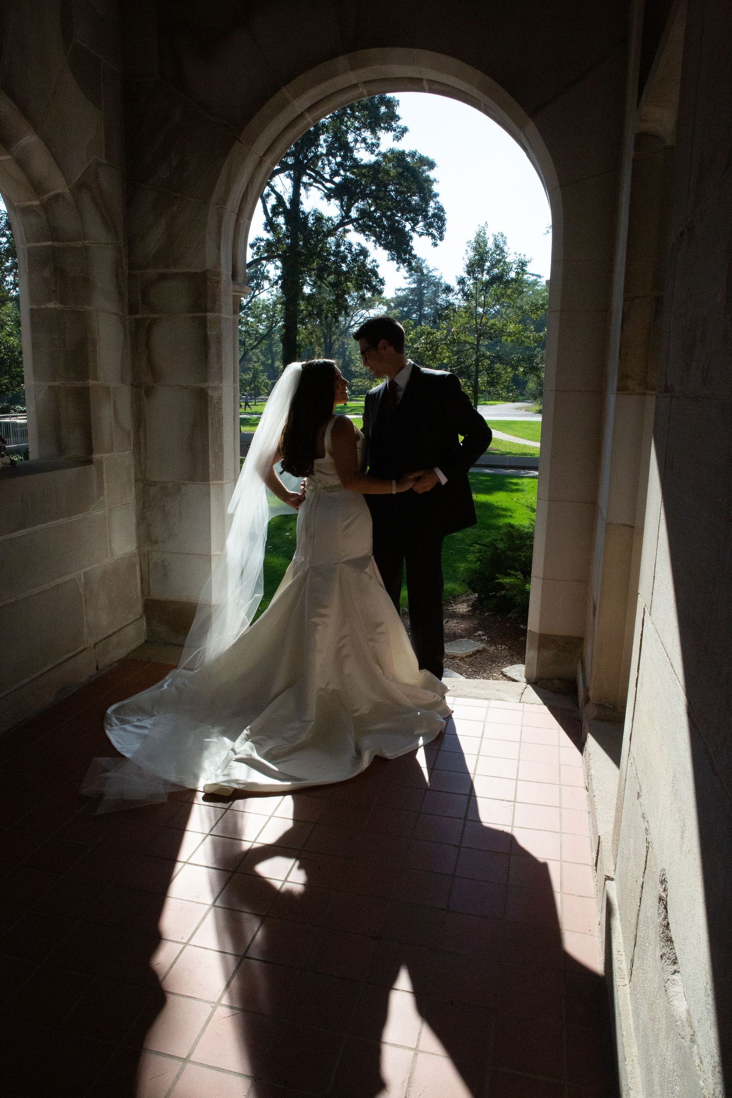 Silhouetted bride and groom share intimate moment under stone archway.