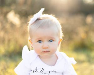 Baby with bright blue eyes photographed in golden sunlight outdoors.