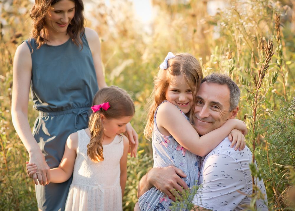 little girl hugs her dad around his neck while mom holds hand of her sister
