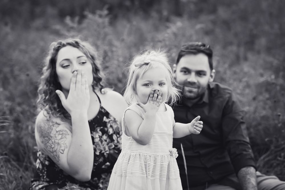 black and white of young family of three blowing kisses at the camera