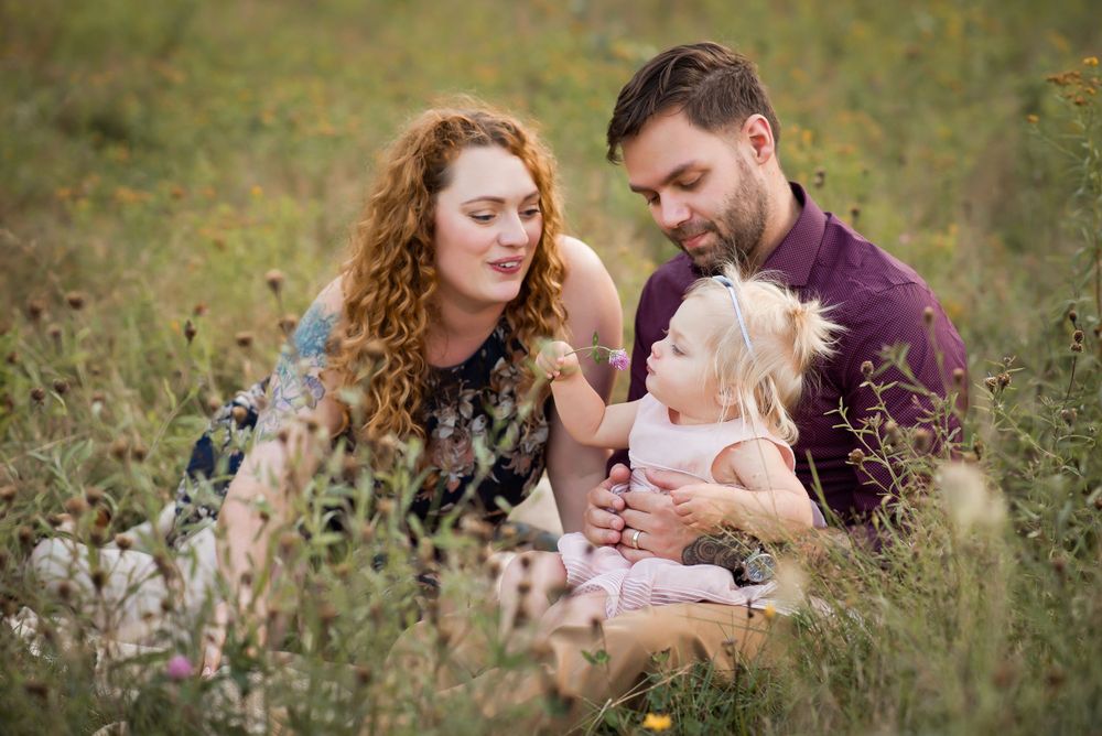 sweet little family in a field with little girl giving her mom a flower