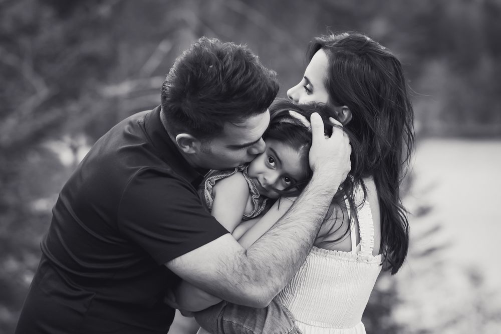 beautiful black and white photo of mom and dad holding and snuggling little girl in outside setting