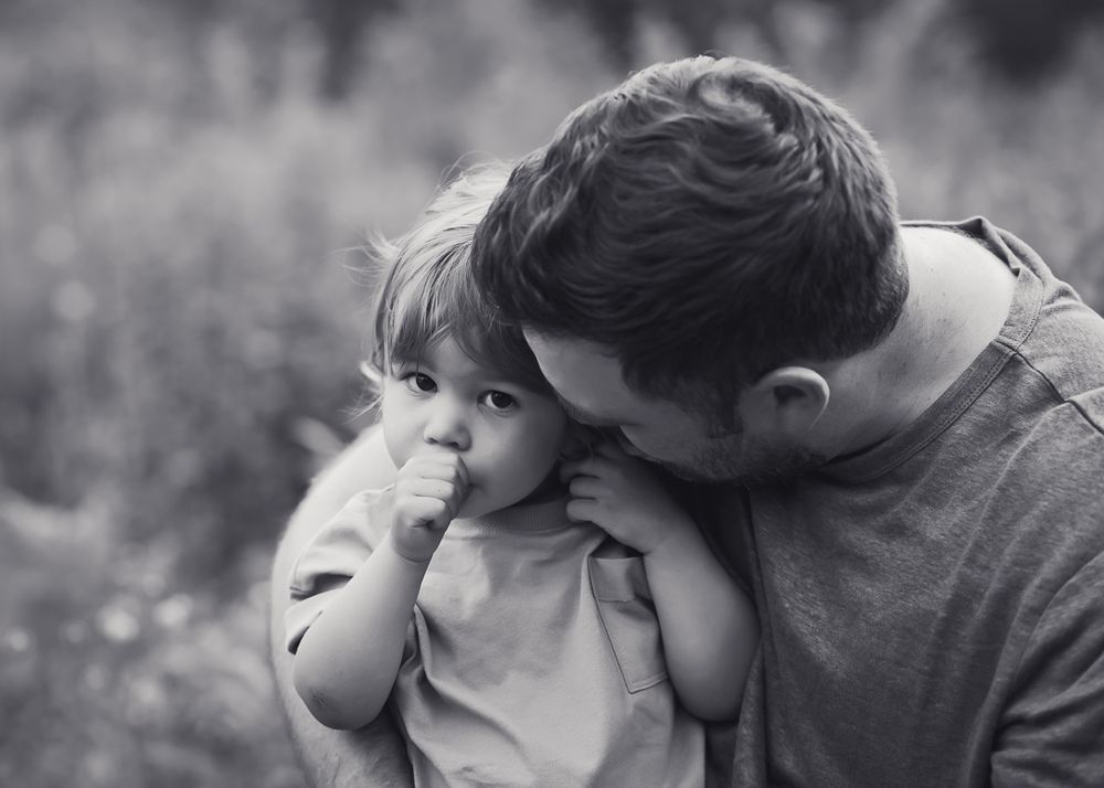 toddler boy snuggles into dad while sucking his thumb